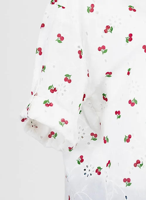 White 100% cotton Cherry Kiss summer shirt with red cherry print, eyelet details, and rolled short sleeves.