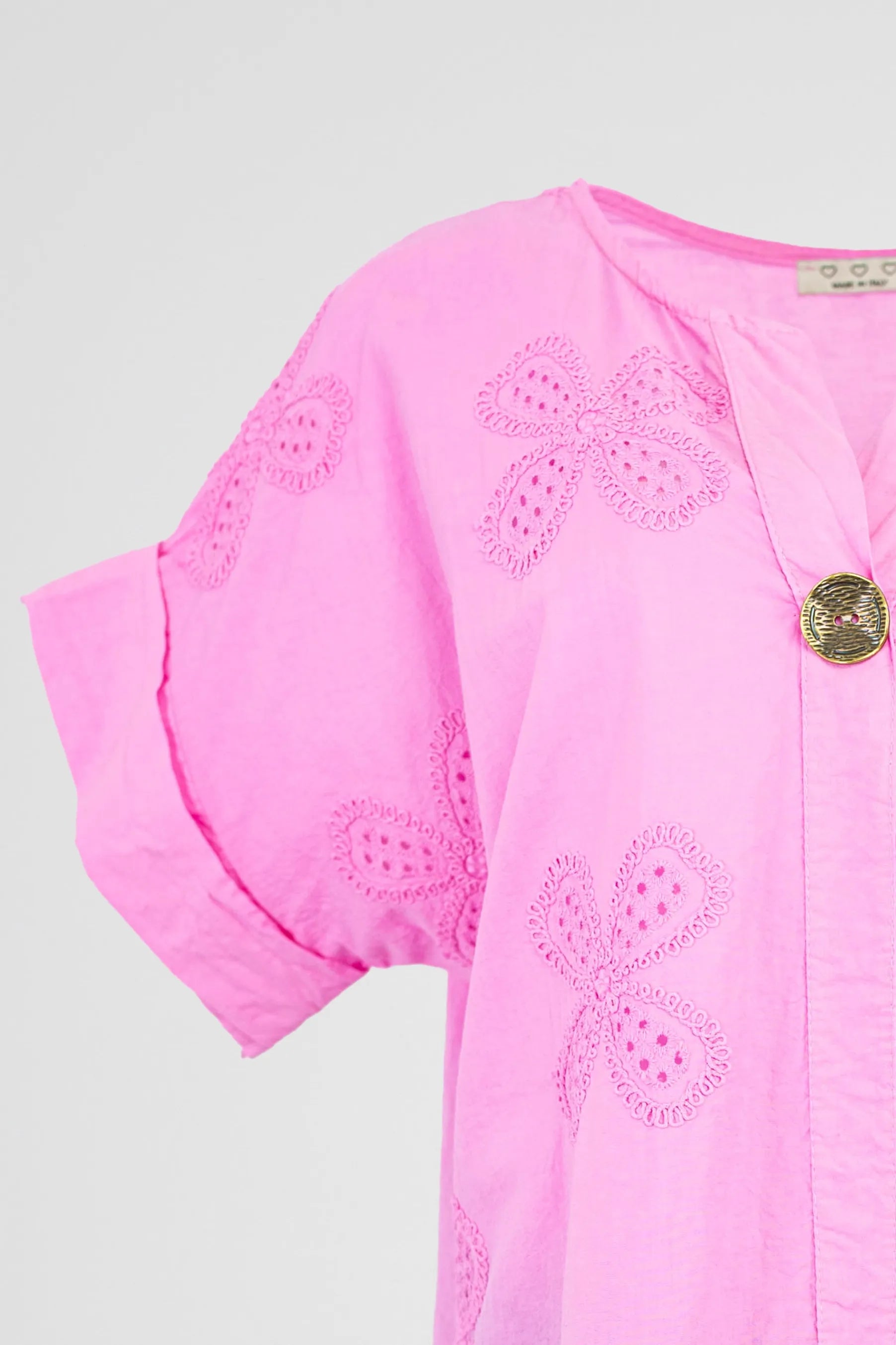 Vibrant pink cotton Bloom Lace shirt with short sleeves, delicate floral eyelet embroidery, and a decorative gold button.