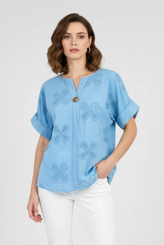 Stylish woman in a light blue cotton Bloom Lace shirt with intricate floral cutouts, short rolled sleeves, and a single button.