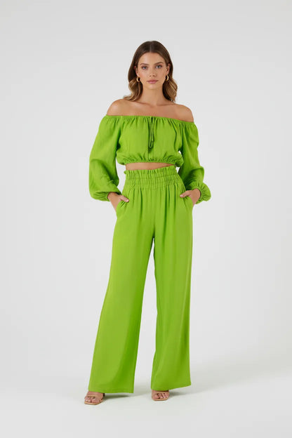 Stylish woman in a vibrant green linen off-shoulder crop top and high-waisted wide-leg pants.