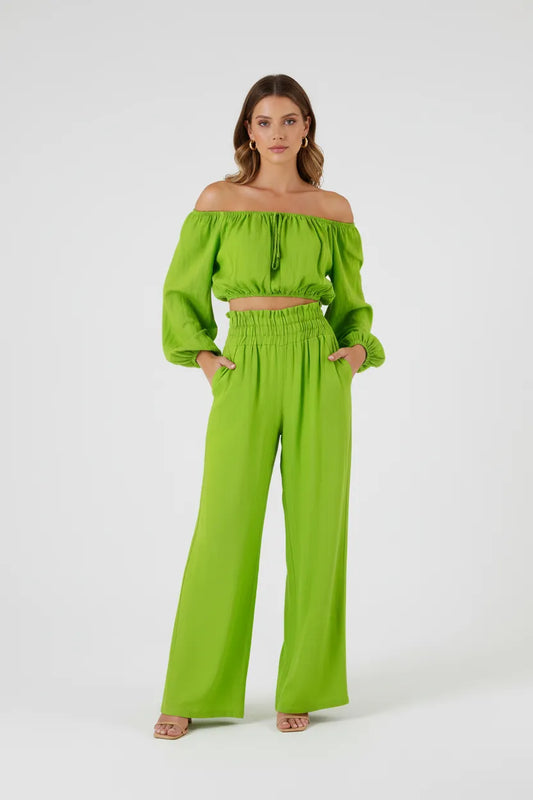 Stylish woman in a vibrant green linen off-shoulder crop top and high-waisted wide-leg pants.
