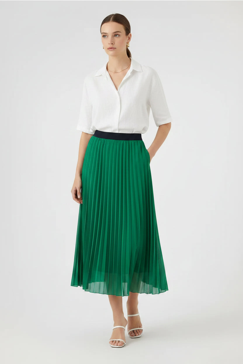 Elegant pleated midi skirt in rich green with a black elastic waistband, paired with a black shirt and boots.