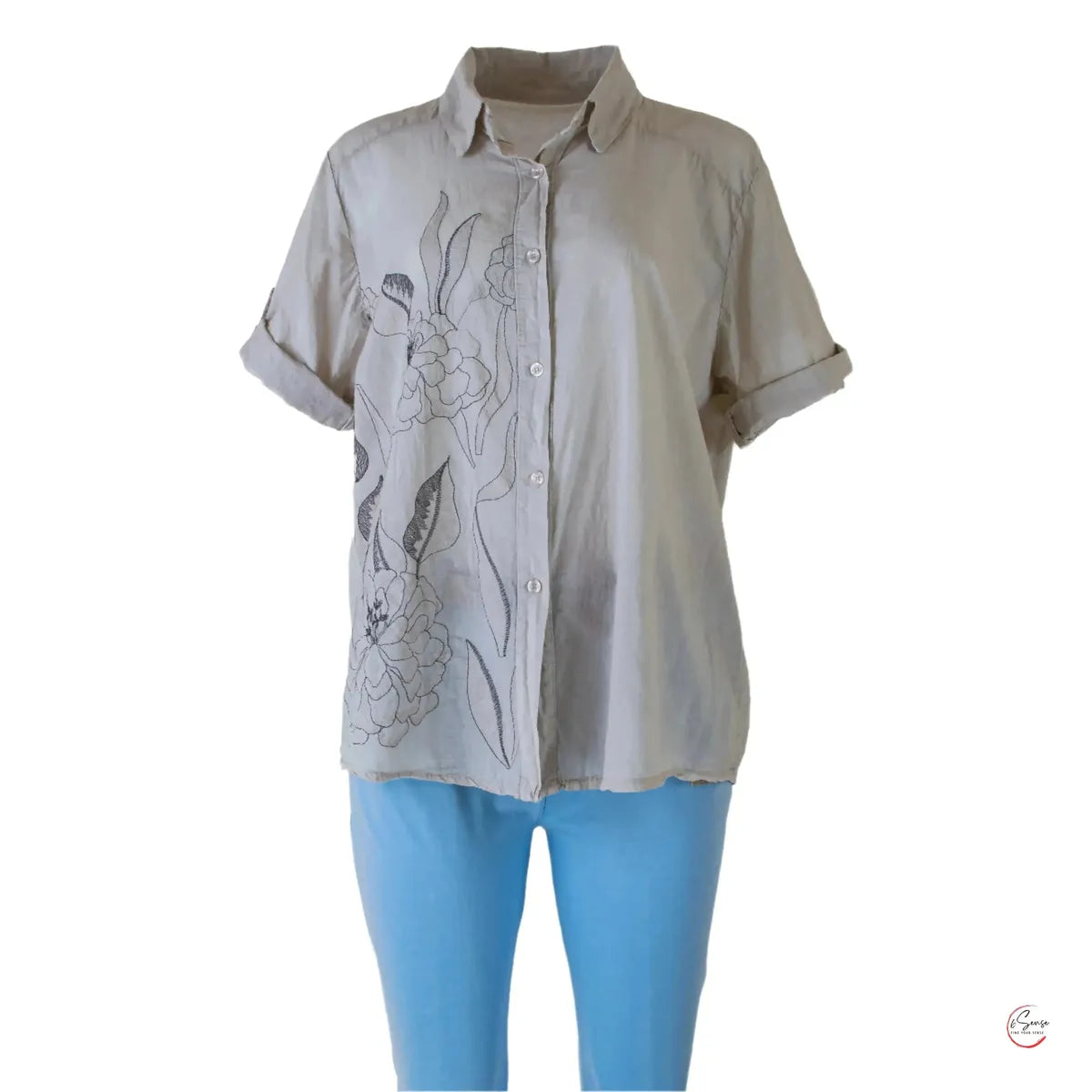 Elegant beige 100% cotton women's shirt with rolled short sleeves and delicate floral embroidery, paired with blue pants.