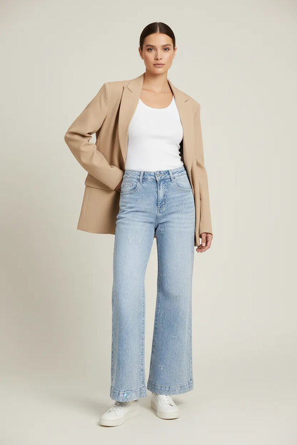 Дамски светлосини дънки Bow Whisper с широк крачол и фини бродирани панделки, съчетани с бял топ и бежово сако.