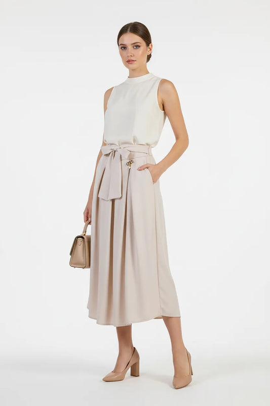 Елегантна дълга бежова пола с панделка, странични джобове и златист детайл, съчетана с бял топ.