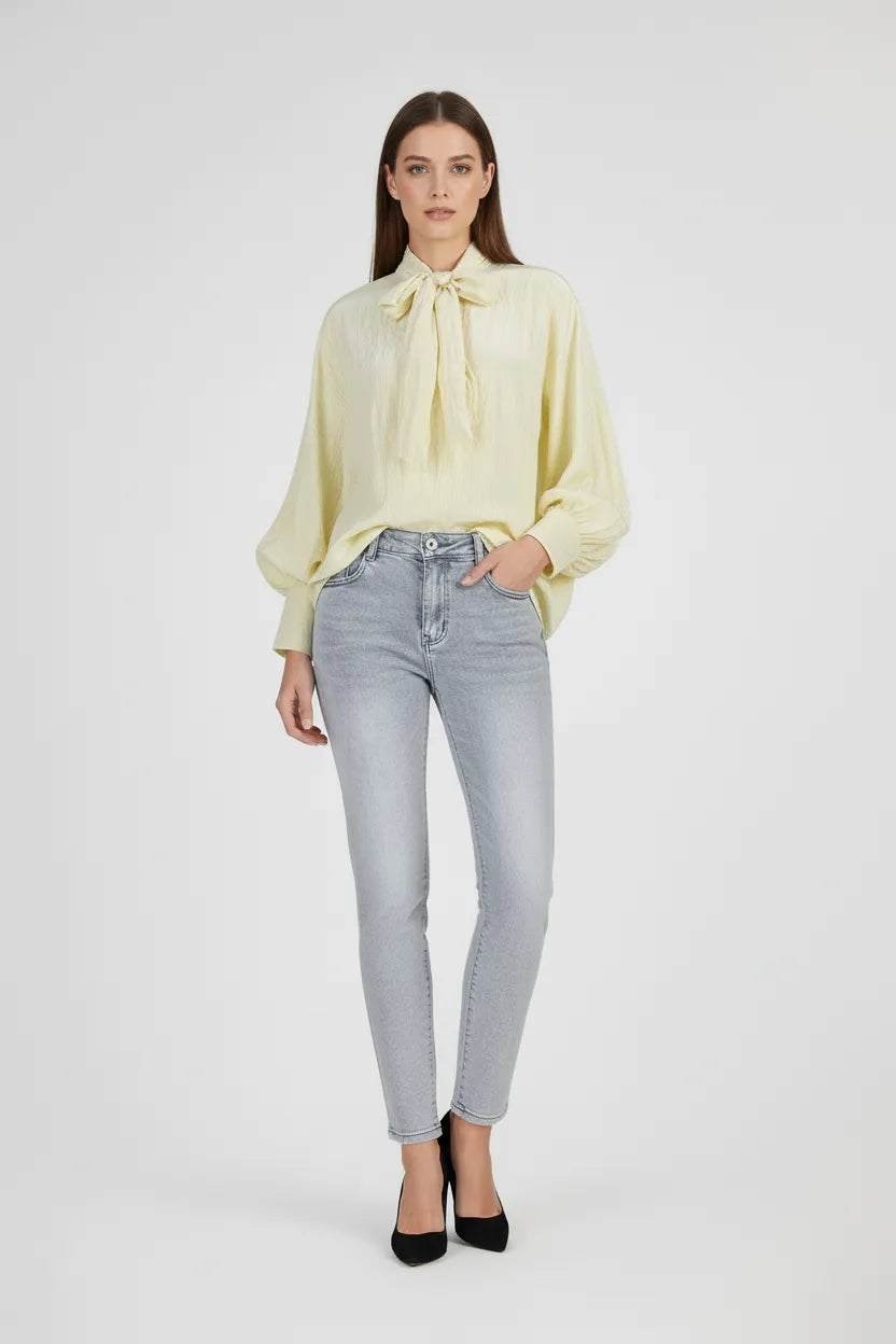 Модел носи Vanilla Denim Set: жълта блуза с панделка и светли, еластични деним дънки.