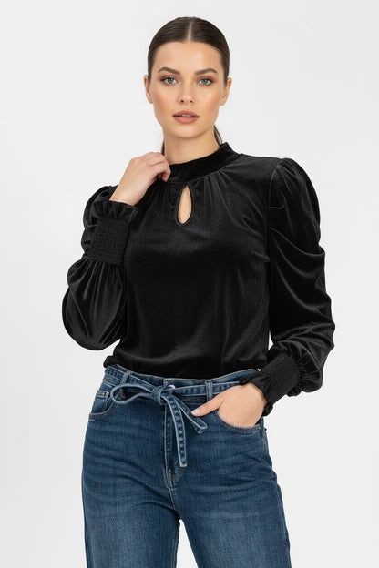 Елегантна черна кадифена блуза с висока яка и дискретен отвор, съчетана с деним дънки с връзка.