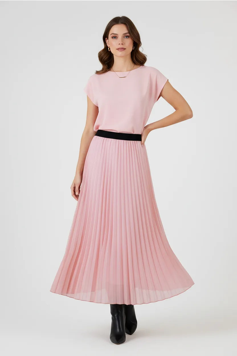 Elegant model in a flowing pink pleated midi skirt with a black elastic waistband and matching pink top.